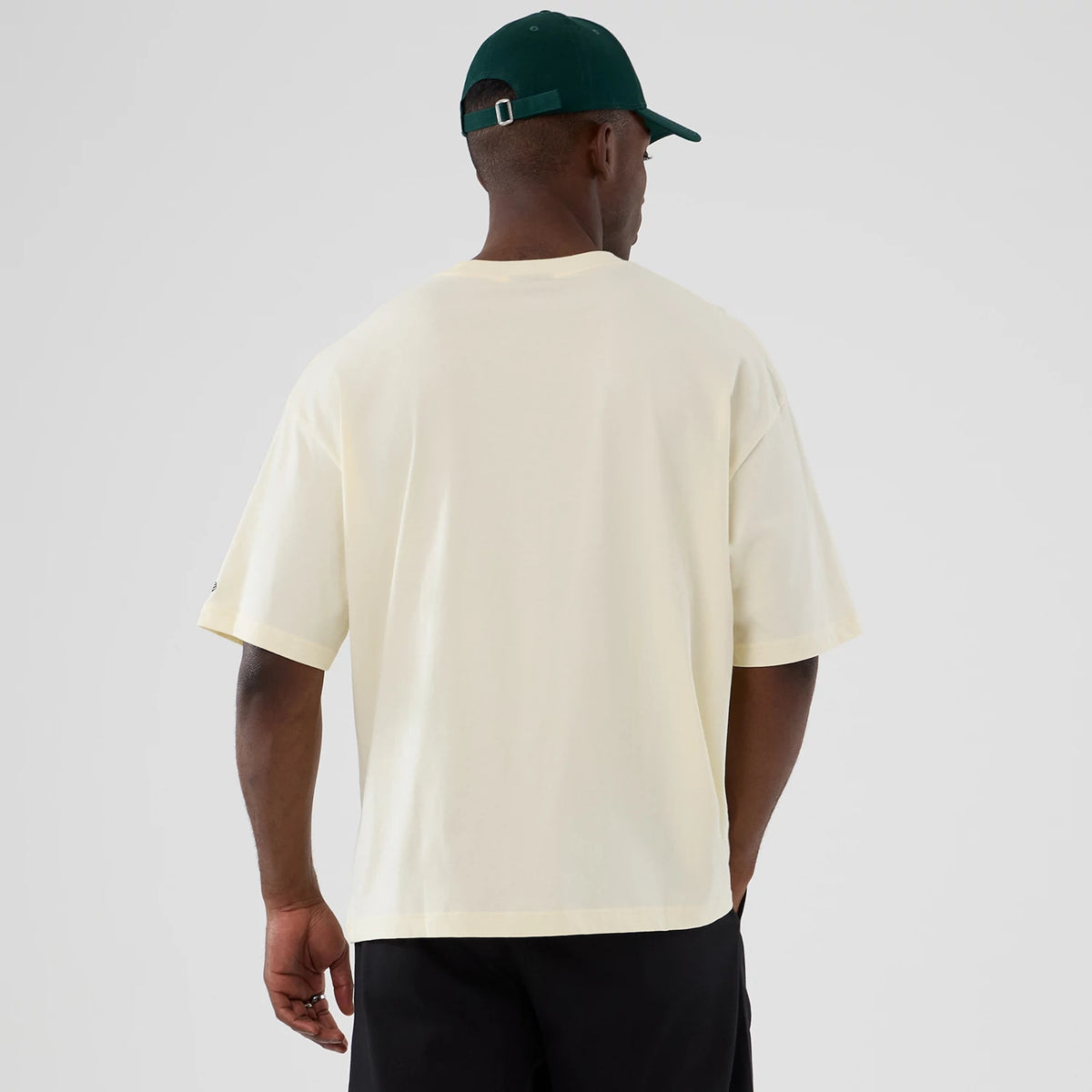 New Era Boston Celtics NBA Hardwood Classic Cream T-Shirt, back view showing the plain cream back of the shirt with short sleeves, worn by a model styled with a dark green cap.