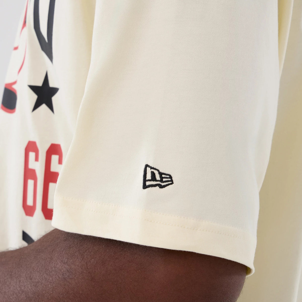 New Era Chicago Bulls NBA Hardwood Classic Cream T-Shirt, side view showing the left sleeve with a black embroidered New Era logo, part of the red number 66 and black star motif on the body of the cream-coloured tee.