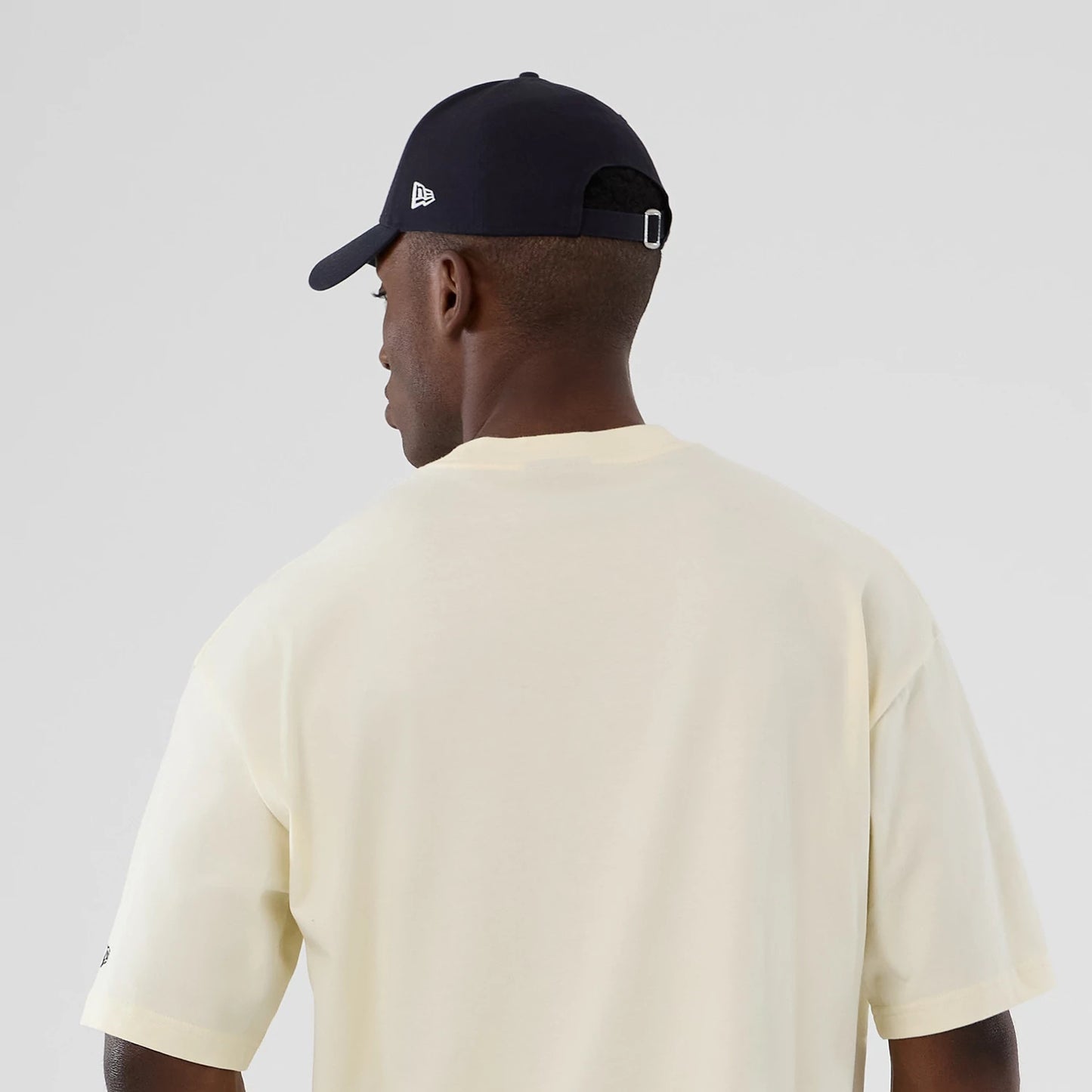 New Era Denver Nuggets NBA Hardwood Classic Cream T-Shirt, back view on-model showing the plain cream back with short sleeves, paired with a navy cap featuring an embroidered New Era logo on the side.