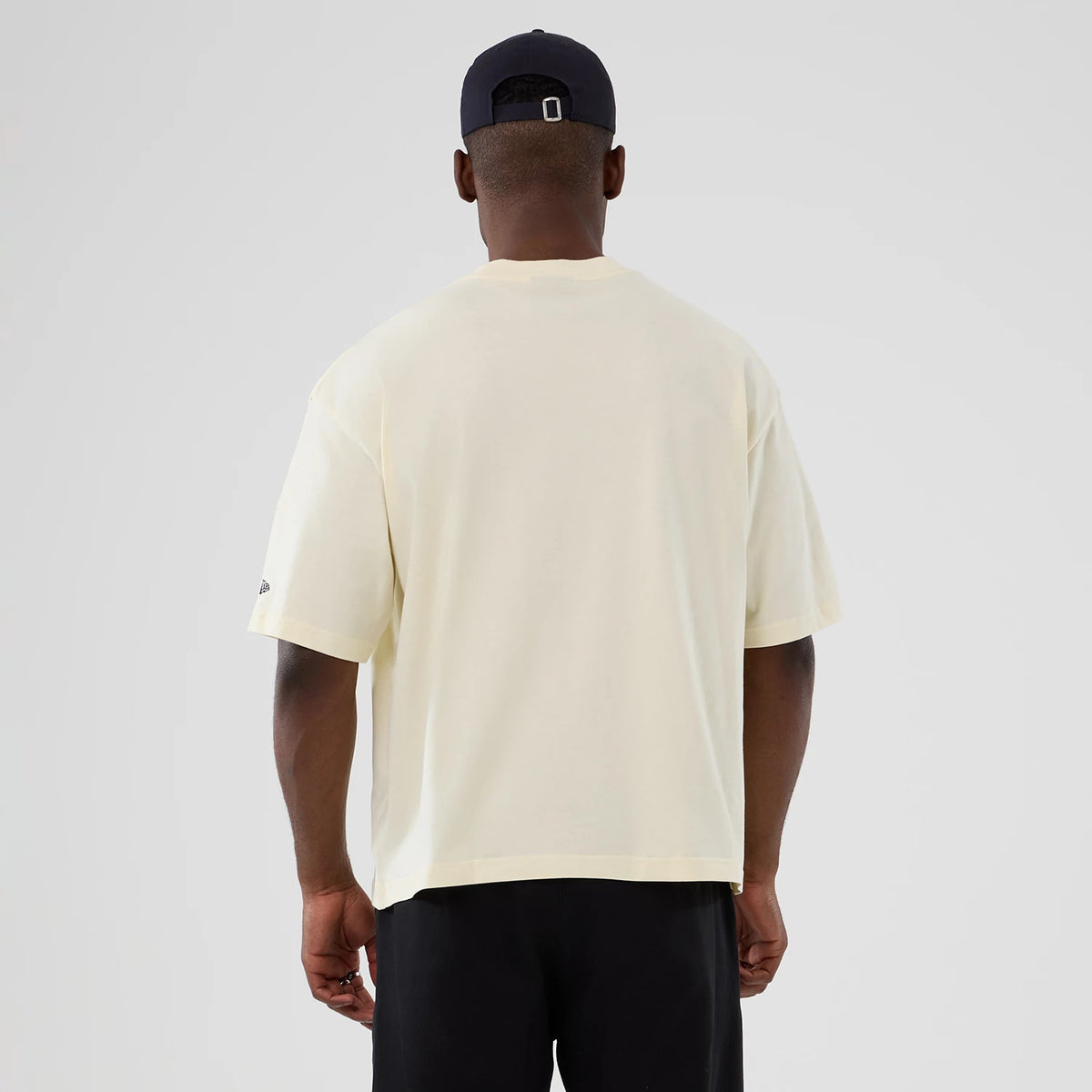 New Era Denver Nuggets NBA Hardwood Classic Cream T-Shirt, back view on a model wearing black shorts and a cap, showing an uninterrupted cream surface with a small embroidered New Era logo on the left sleeve near the cuff.