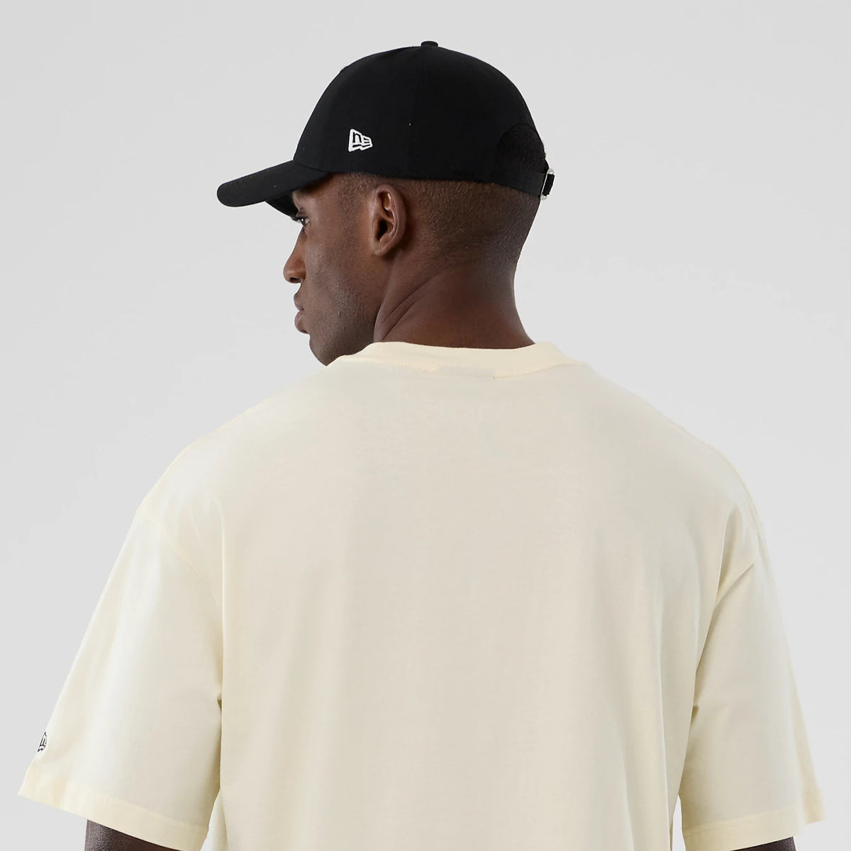 New Era LA Lakers NBA Hardwood Classic Cream T-Shirt, back view on-model showing the plain cream fabric with short sleeves, a small embroidered New Era logo in black on the left sleeve.