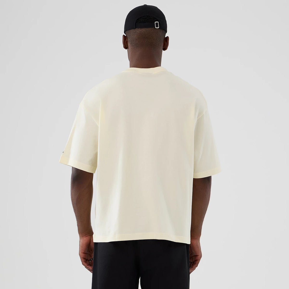 New Era Vancouver Grizzlies NBA Hardwood Classic Cream T-Shirt, back view on-model paired with a black cap, displaying a minimalist cream design with short sleeves and a relaxed fit, no logos or graphics from this angle.