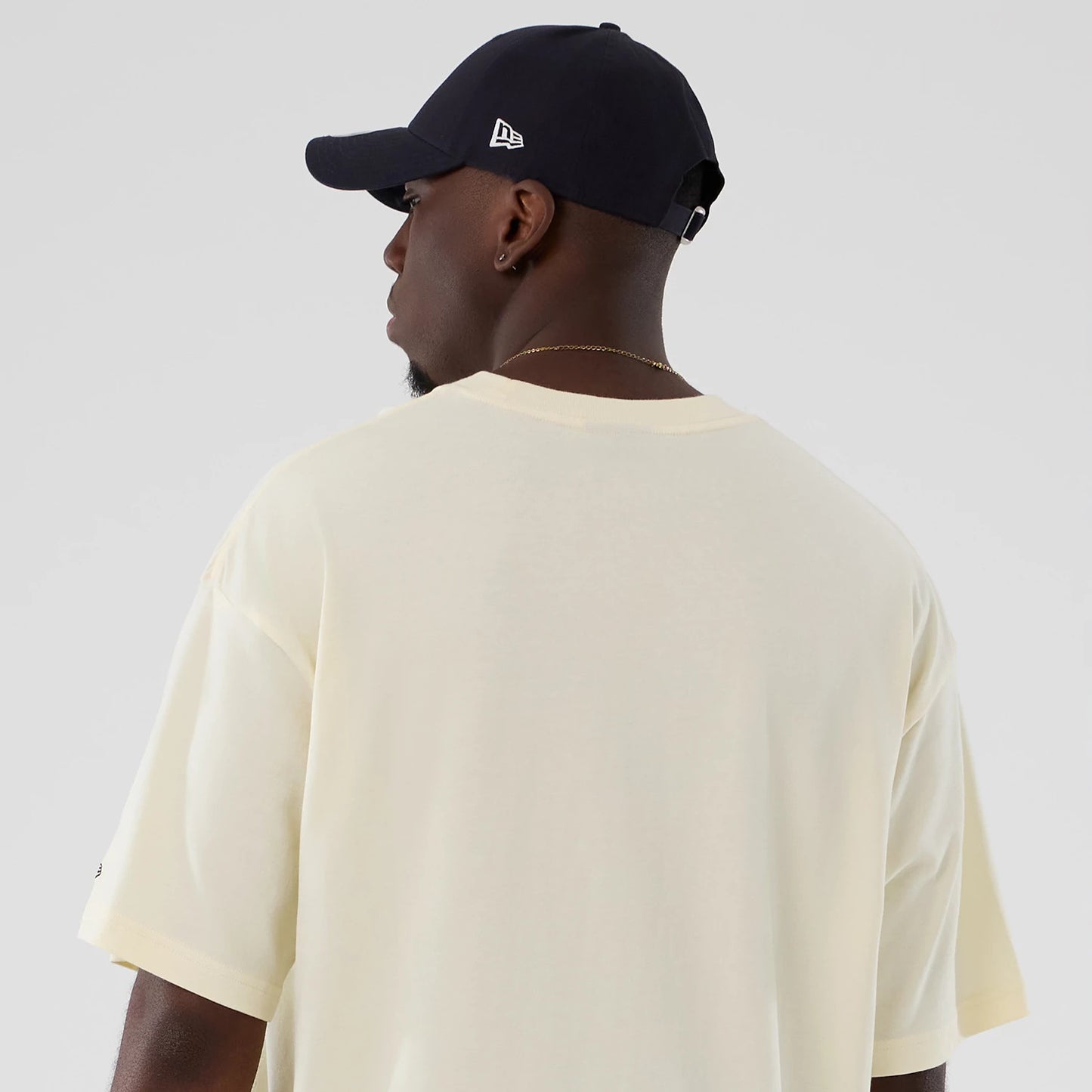 New Era Utah Jazz NBA Hardwood Classic Cream T-Shirt, back view on a model also wearing a dark cap, showing the plain cream oversized tee with loose short sleeves and stitch along the shoulders.