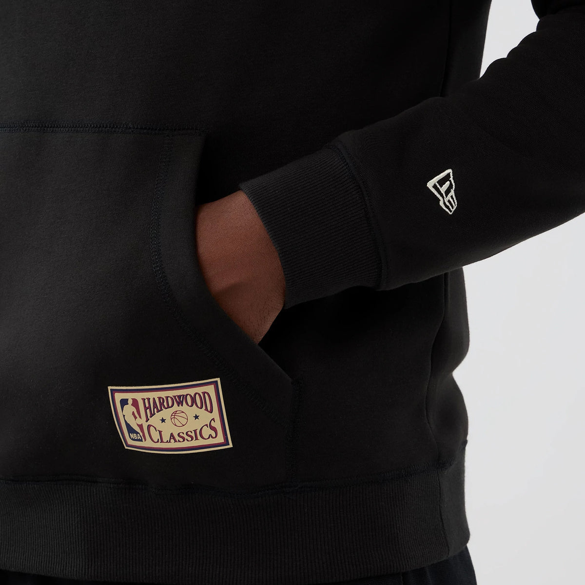 New Era LA Lakers NBA Hardwood Classic Black Pullover Hoodie, front view showing a beige embroidered NBA Hardwood Classics patch near the lower pocket and a white embroidered New Era logo on the sleeve cuff.