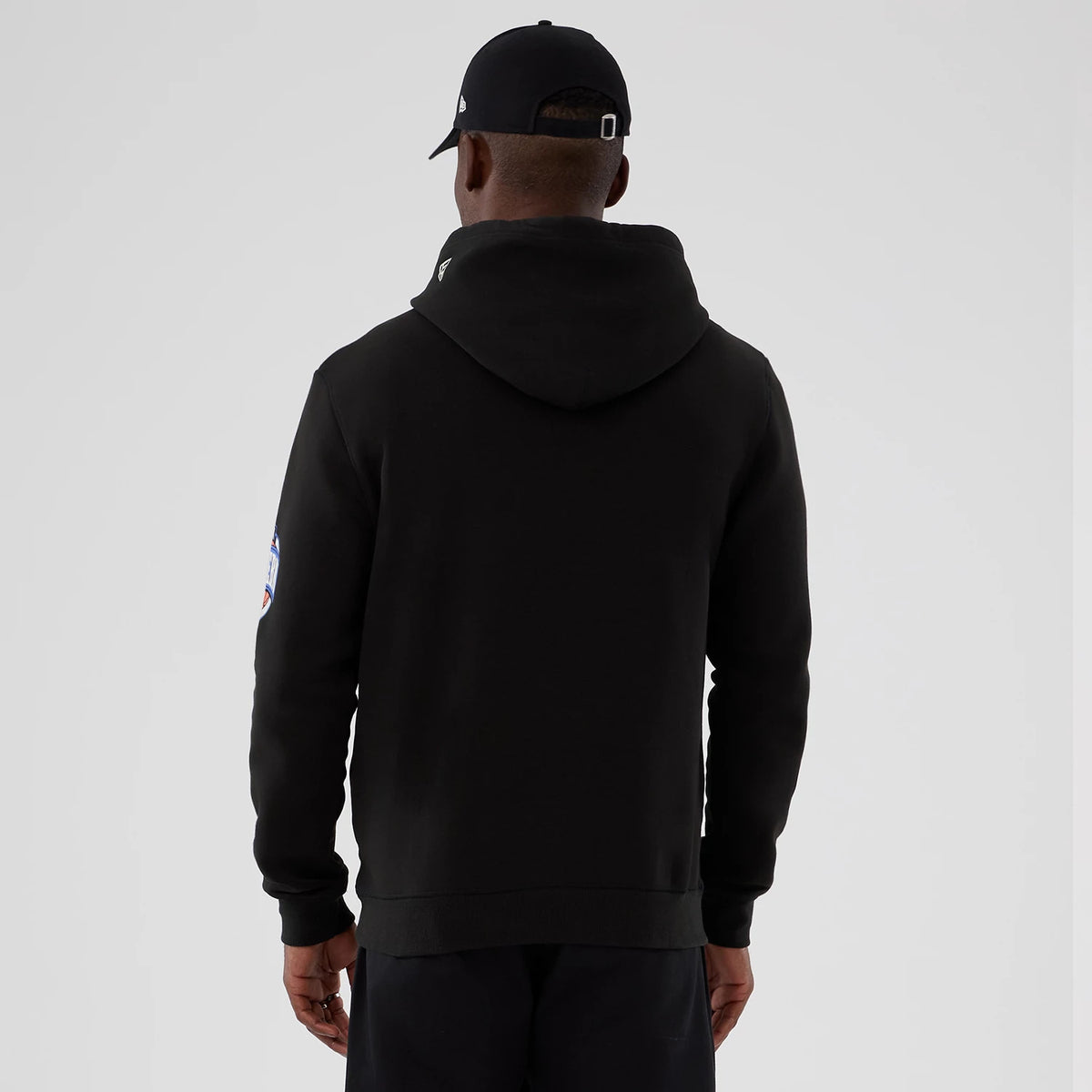 New Era Chicago Bulls NBA Hardwood Classic Black Pullover Hoodie, back view on a model with a black cap, displaying the plain black back and a patch graphic on the sleeve, with a small logo above the hood.