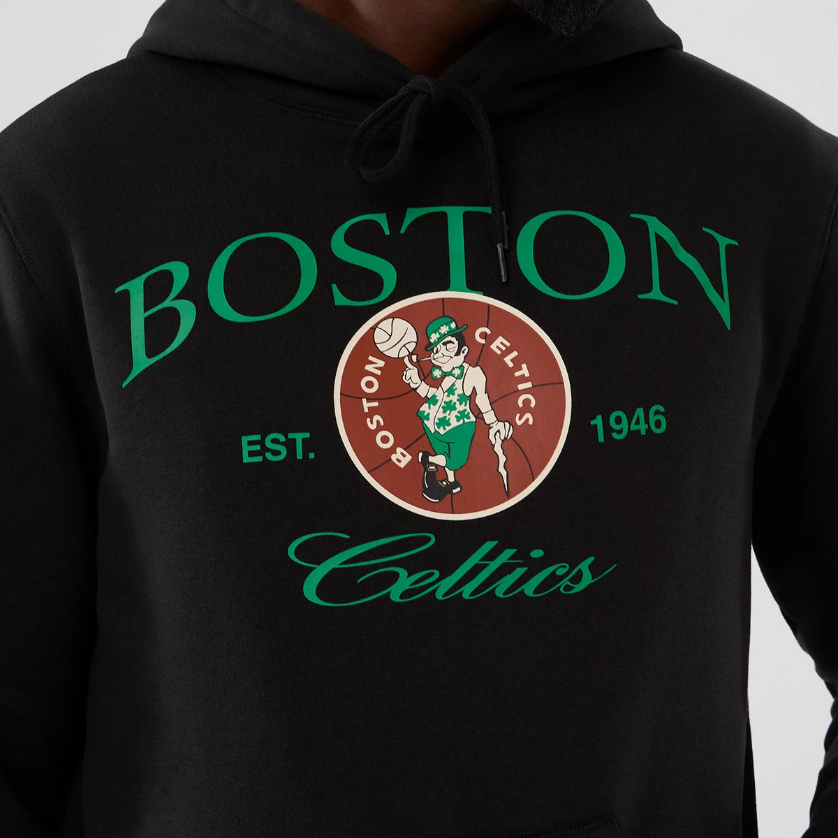 New Era Boston Celtics NBA Hardwood Classic Black Pullover Hoodie, front view featuring green Boston Celtics lettering and a large printed logo with the leprechaun mascot holding a basketball, styled on a model.