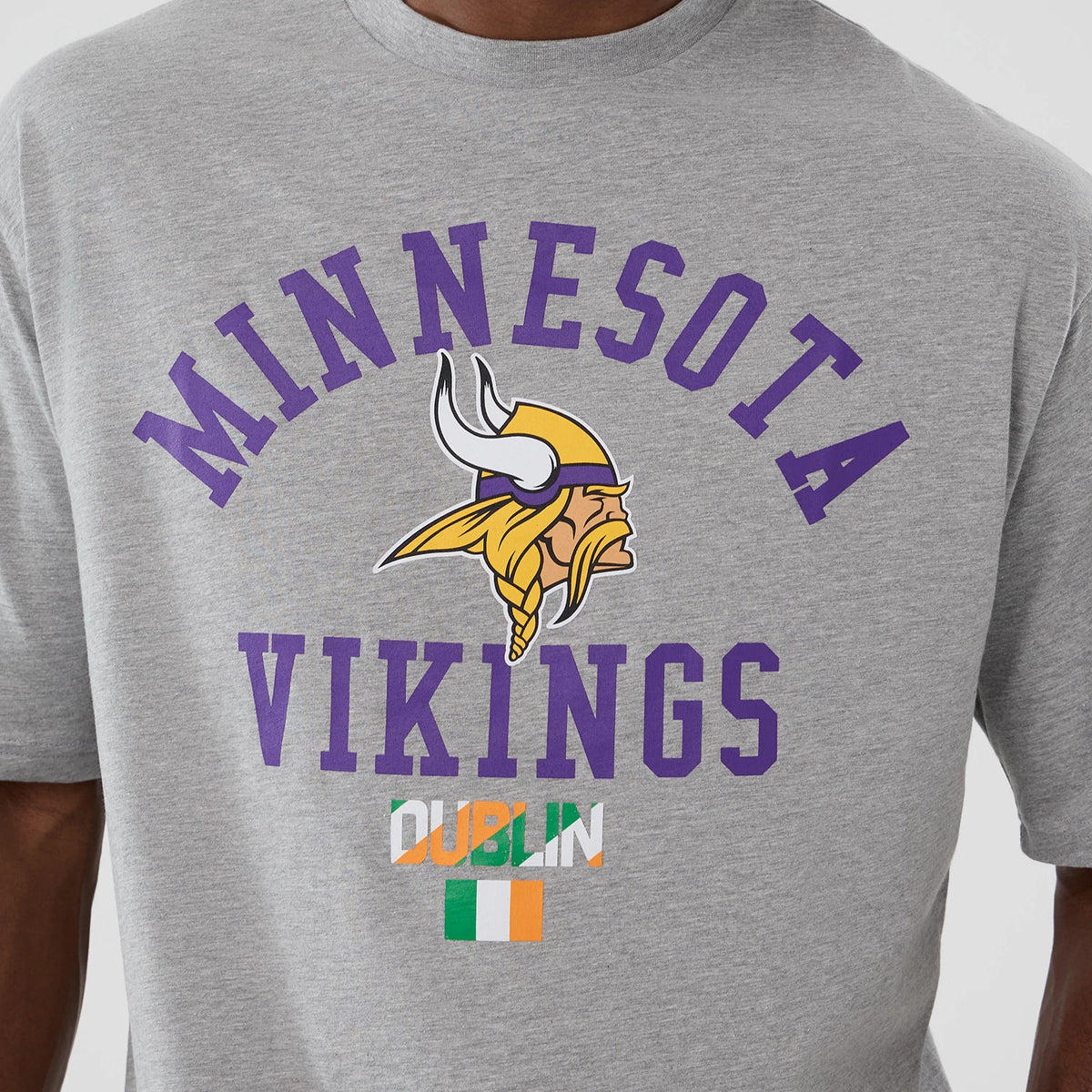 New Era Vikings NFL International Series Games Dublin 2025 Grey Oversized T-Shirt, front view displaying a purple Minnesota Vikings lettering with a Viking logo and Dublin text, featuring the Irish flag graphic on a light grey background.