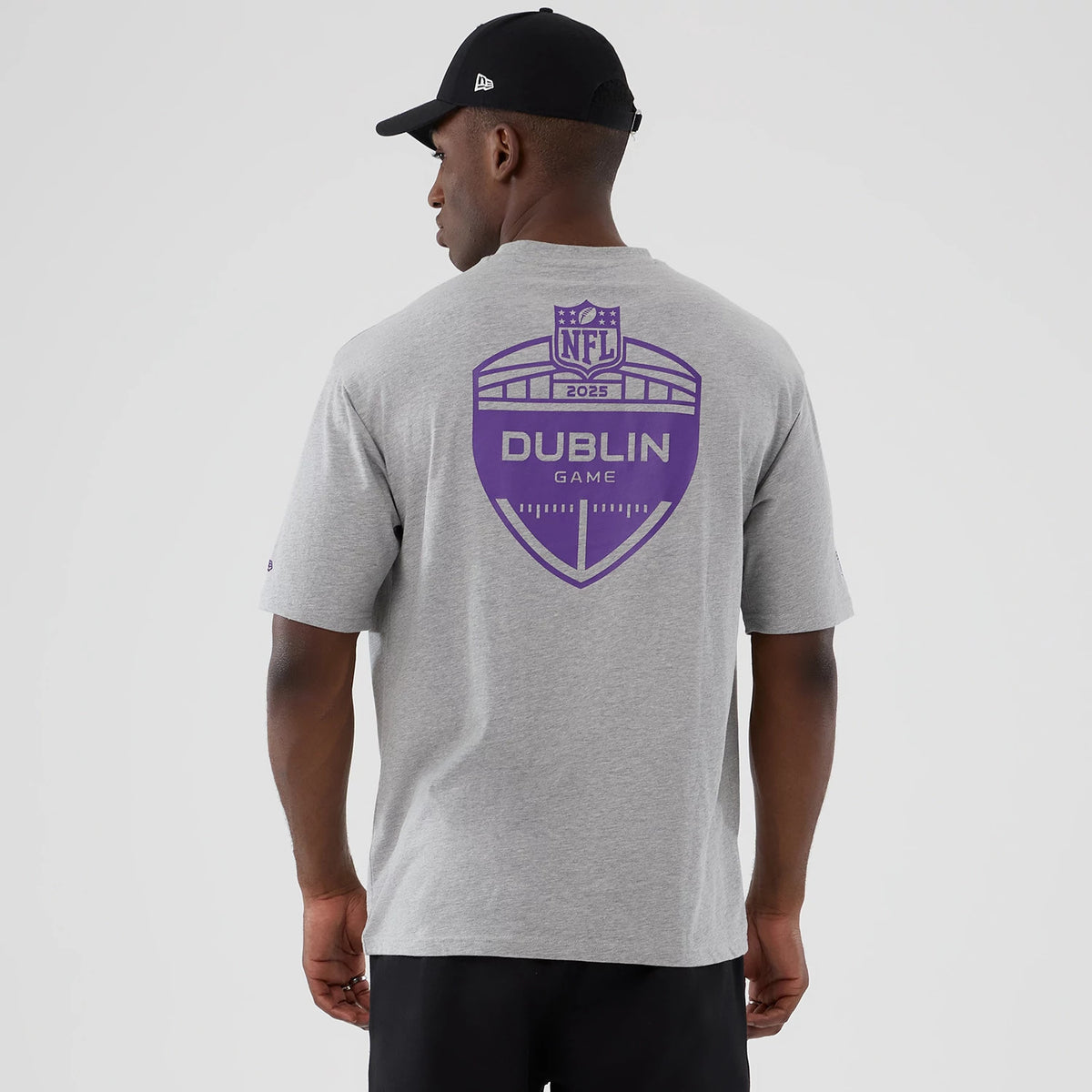 New Era Vikings NFL International Series Games Dublin 2025 Grey Oversized T-Shirt, back view on a model showing a large purple printed crest with NFL 2025 and Dublin Game text, contrasting against the light grey fabric.