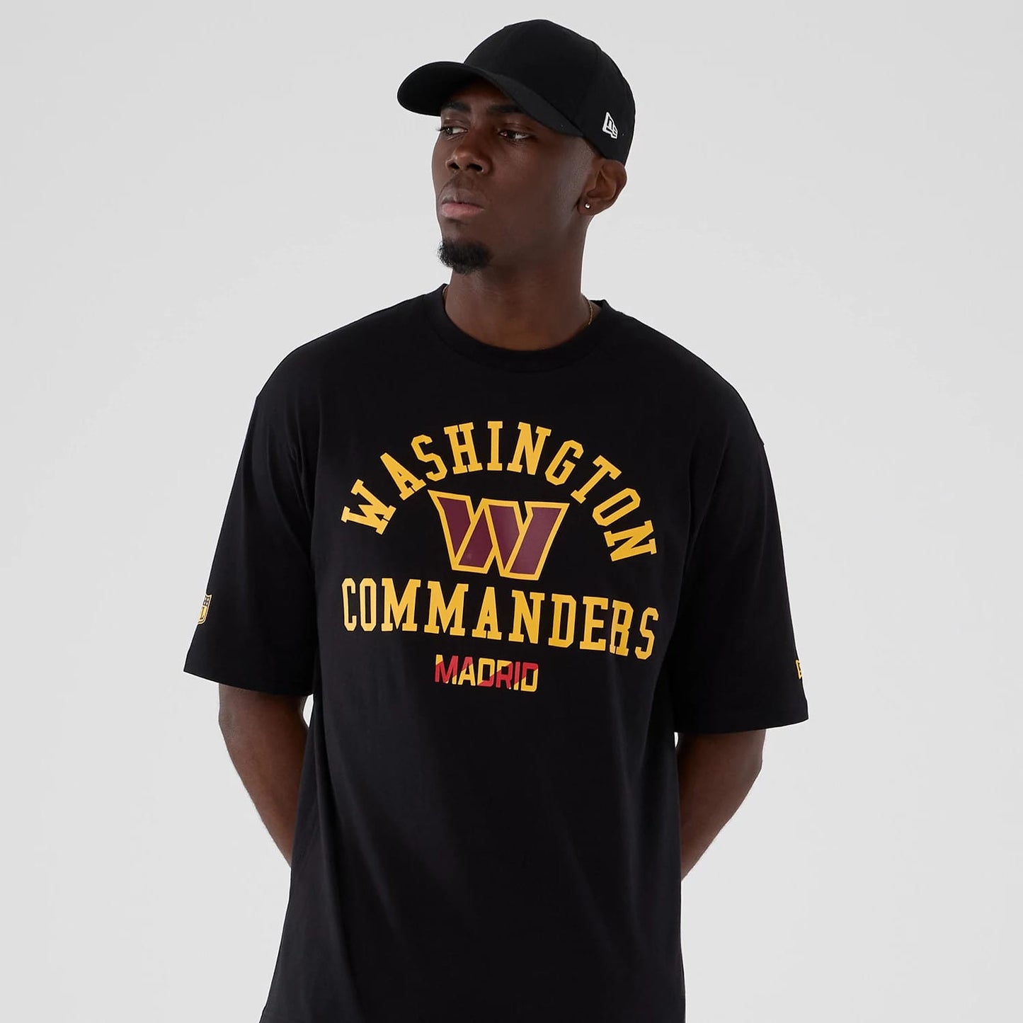 New Era Washington Commanders NFL International Series Games 2025 Black Oversized T-Shirt, front view on-model showing yellow Washington Commanders lettering and logo on the chest, Madrid printed beneath, New Era logo printed on the sleeve.