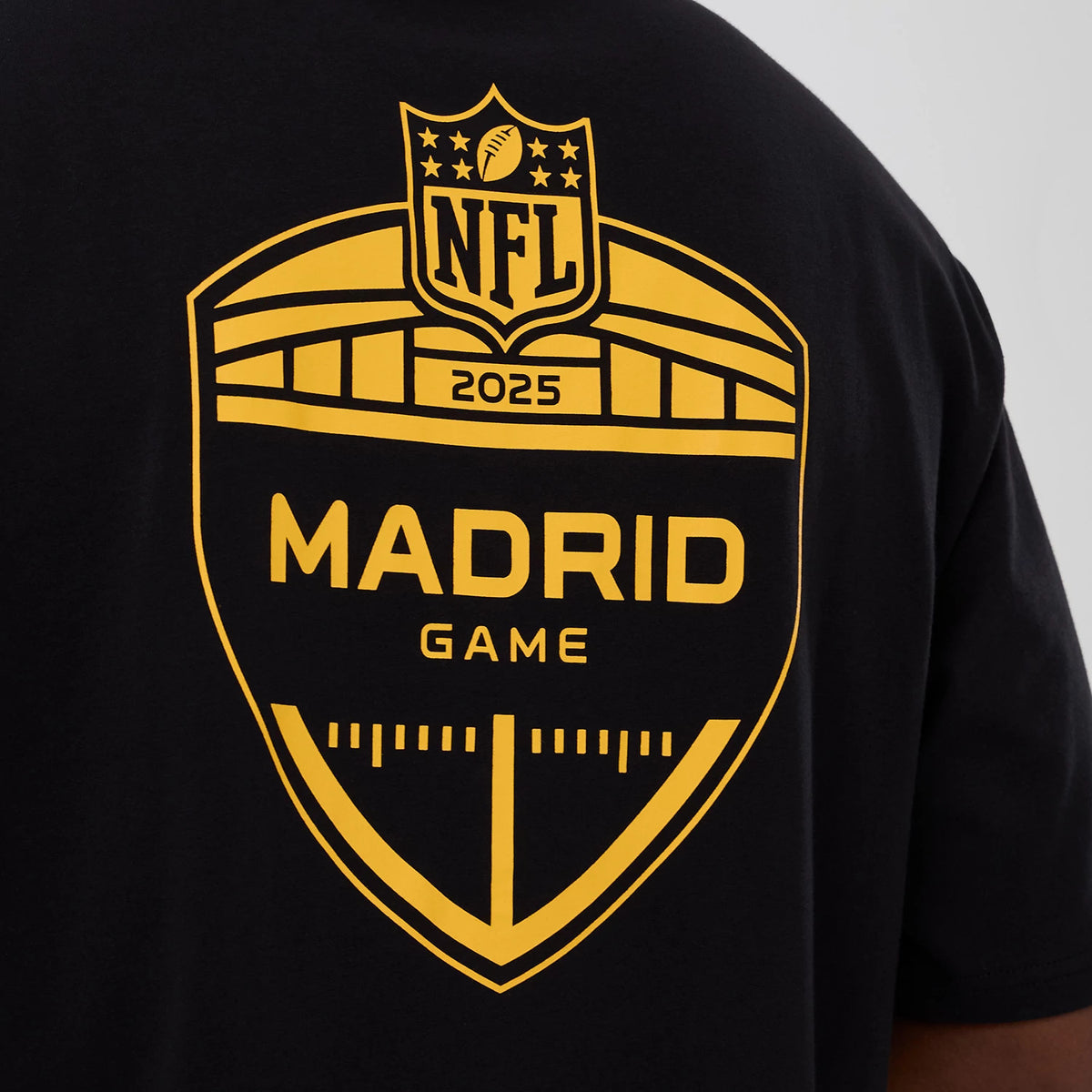 New Era Washington Commanders NFL International Series Games 2025 Black Oversized T-Shirt, back view displaying a yellow printed Madrid Game shield graphic centred on the upper back, featuring NFL and 2025 lettering above a stylised stadium design.