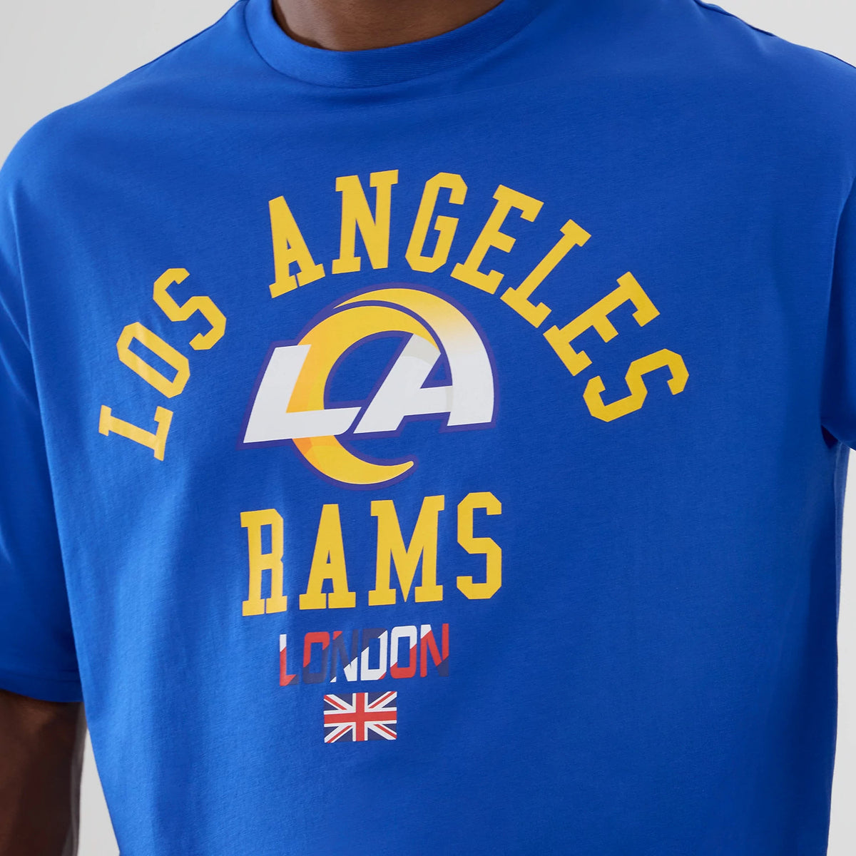 New Era LA Rams NFL International Series Games 2025 Bright Blue Oversized T-Shirt, front view showing Los Angeles Rams lettering in yellow above a large white LA logo, with London text and a Union Jack graphic below it.