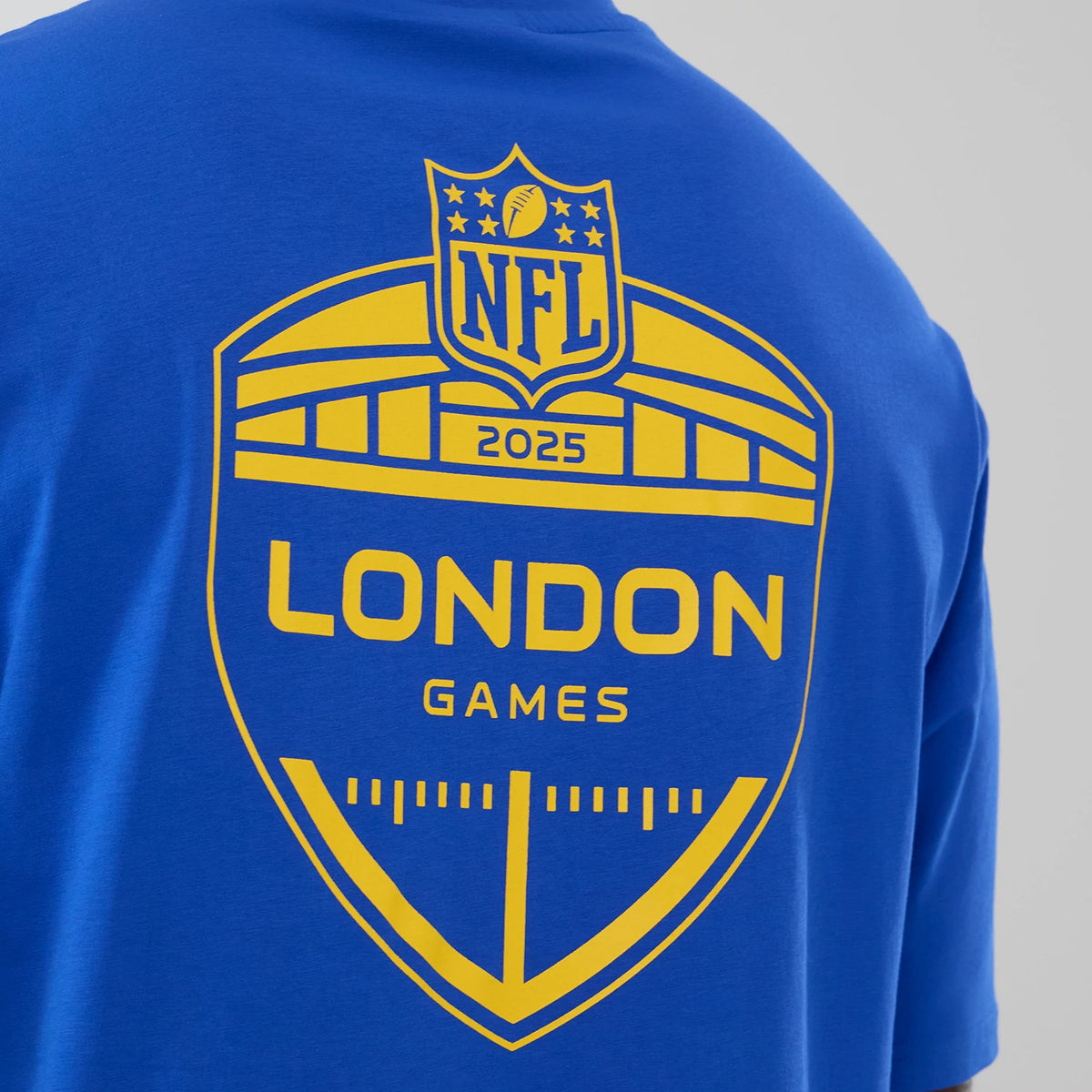 New Era LA Rams NFL International Series Games 2025 Bright Blue Oversized T-Shirt, back view showing a yellow printed shield graphic with NFL 2025 branding and the words London Games across the upper back.