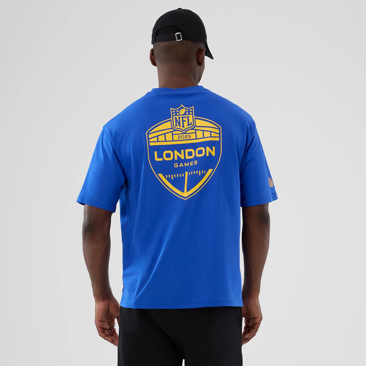 New Era LA Rams NFL International Series Games 2025 Bright Blue Oversized T-Shirt, back view showing a large yellow NFL London Games 2025 graphic centred on the blue fabric, worn by a model with short sleeves and a casual fit.