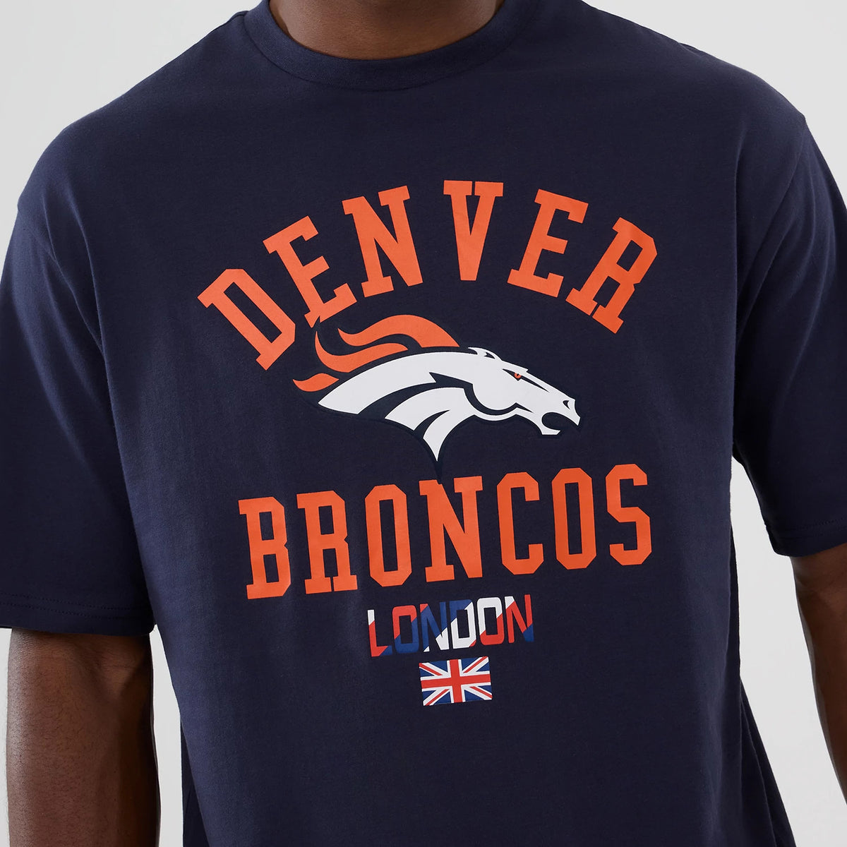 New Era Denver Broncos NFL International Series Games 2025 Navy Oversized T-Shirt, front view showing orange Denver Broncos lettering and logo centred on the chest, with London lettering and a Union Jack flag graphic beneath.