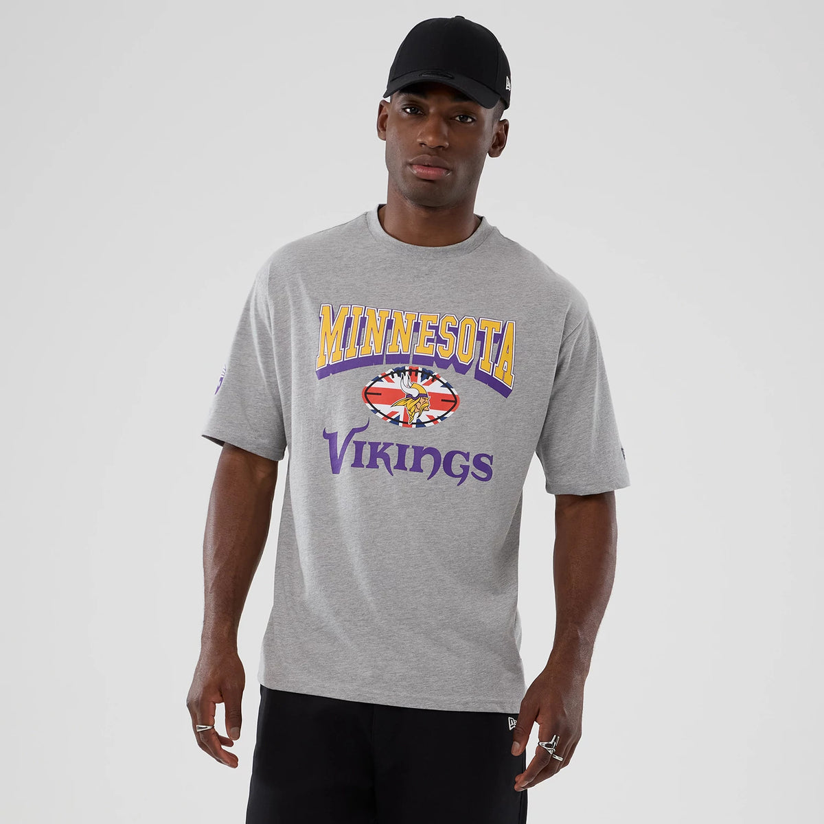 New Era Vikings NFL International Series Games London 2025 Grey Oversized T-Shirt, front view on-model showing the decorative Vikings graphic on the chest with yellow Minnesota lettering above and a small New Era logo embroidered on the left sleeve.
