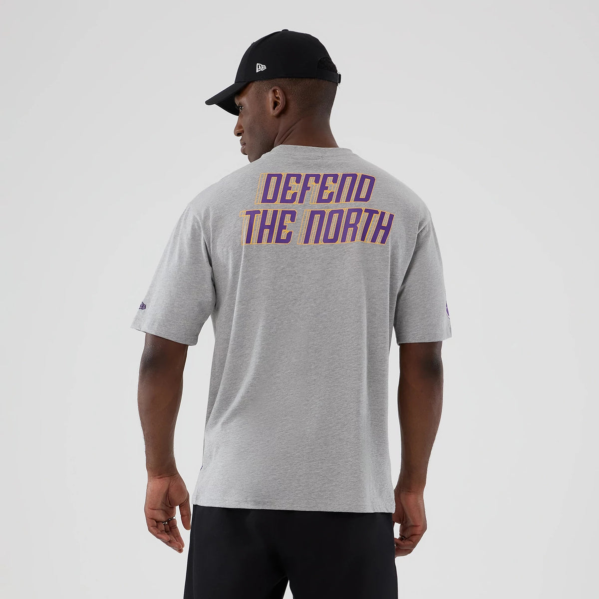 New Era Vikings NFL International Series Games London 2025 Grey Oversized T-Shirt, back view on a model wearing a black cap, featuring purple and gold lettering DEFEND THE NORTH across the upper back centre.