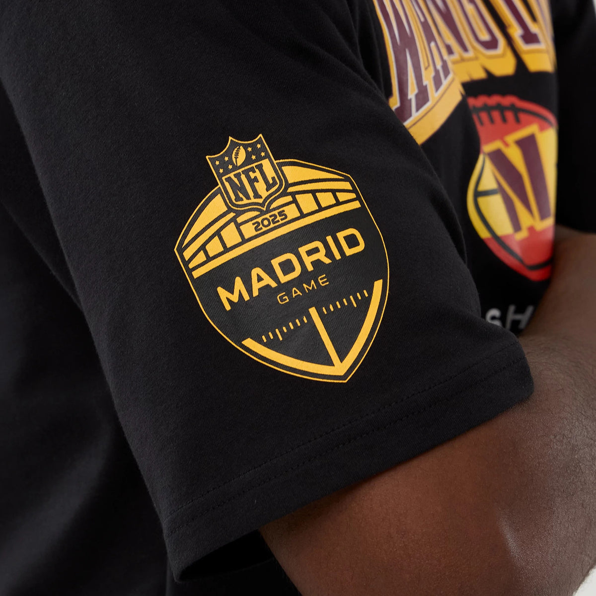 New Era Commanders NFL International Series Games Script 2025 Black Oversized T-Shirt, side view on-model featuring a large yellow printed Madrid Game logo on the sleeve, with NFL graphics on the chest.