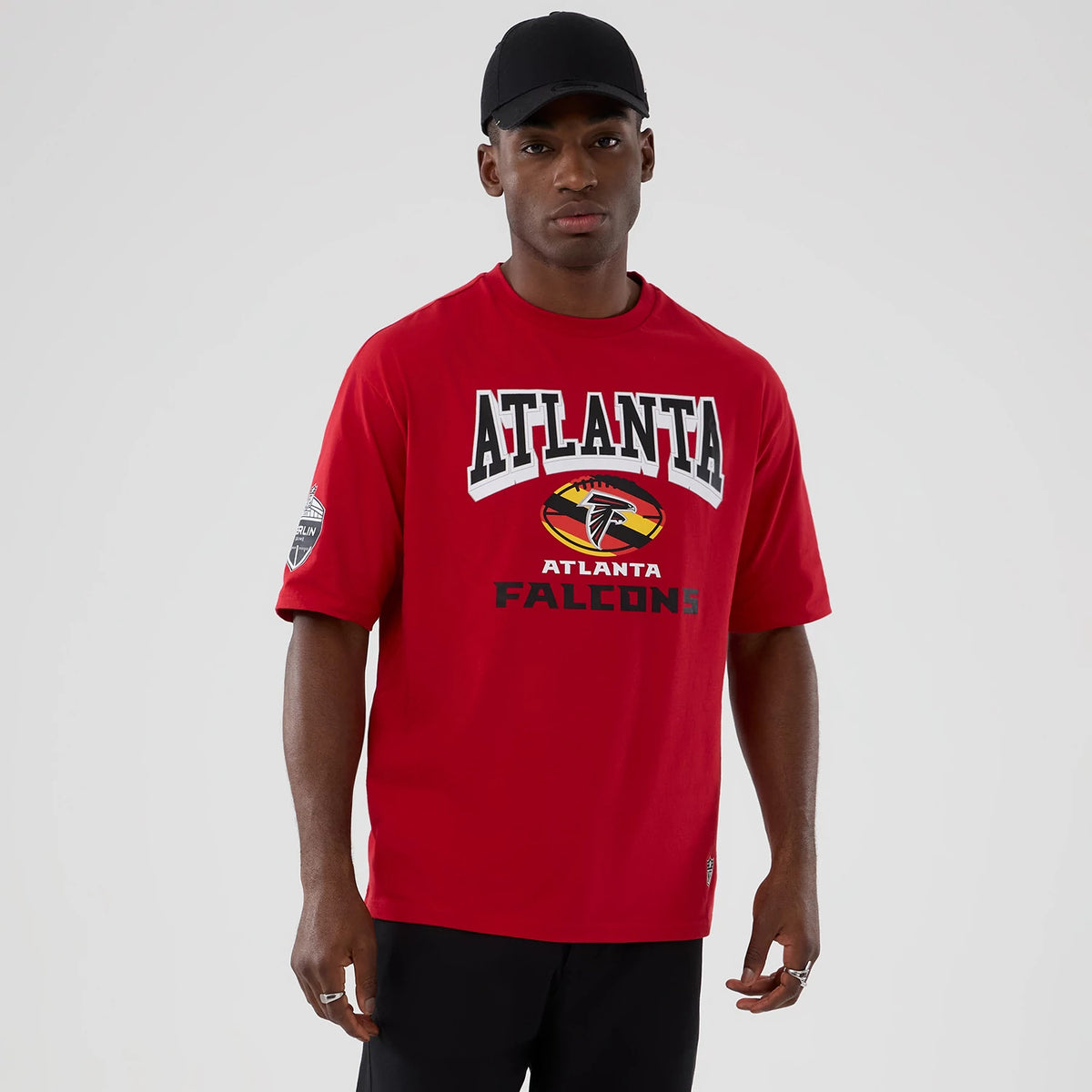 New Era Atlanta Falcons NFL International Series Games 2025 Red Oversized T-Shirt, front view on-model showing large printed ATLANTA FALCONS lettering and team logo on the chest, with an additional logo patch on the left sleeve.