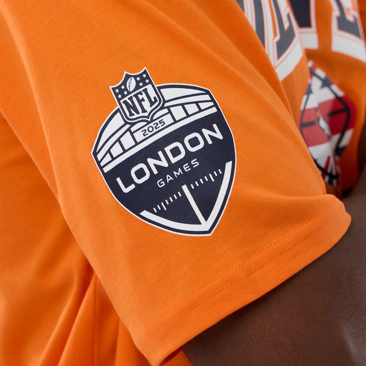 New Era Denver Broncos NFL International Series Games 2025 Orange Oversized T-Shirt, side view showing a detailed printed NFL London Games 2025 logo on the sleeve of the orange fabric, worn casually on a model.
