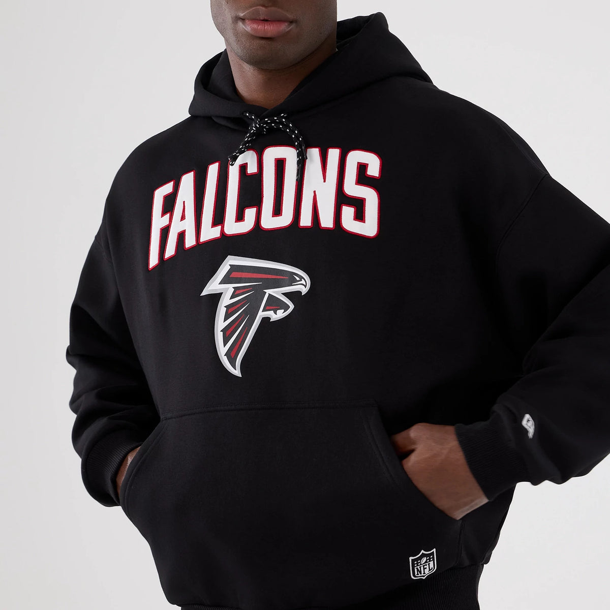 New Era Atlanta Falcons NFL International Series Games 2025 Black Premium Pullover Hoodie, front view showing the white FALCONS lettering and large Atlanta Falcons logo on the chest, with an embroidered New Era flag on the left sleeve.