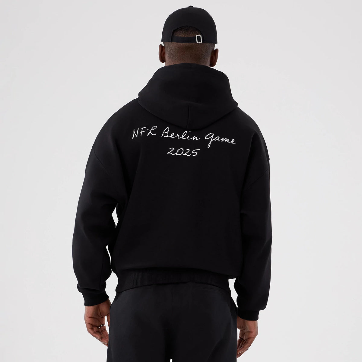New Era Atlanta Falcons NFL International Series Games 2025 Black Premium Pullover Hoodie, back view on a model showing the white printed text NFL Berlin Game 2025 across the upper back, and a relaxed fit with a hood.