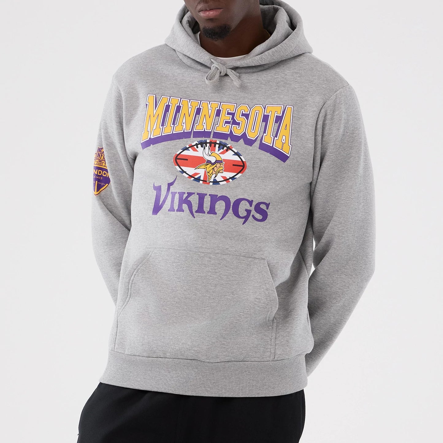 New Era Minnesota Vikings NFL International Series Games 2025 Grey Pullover Hoodie, front view on a model showing a purple and yellow team logo across the chest and a London patch on the left sleeve against a light grey background.