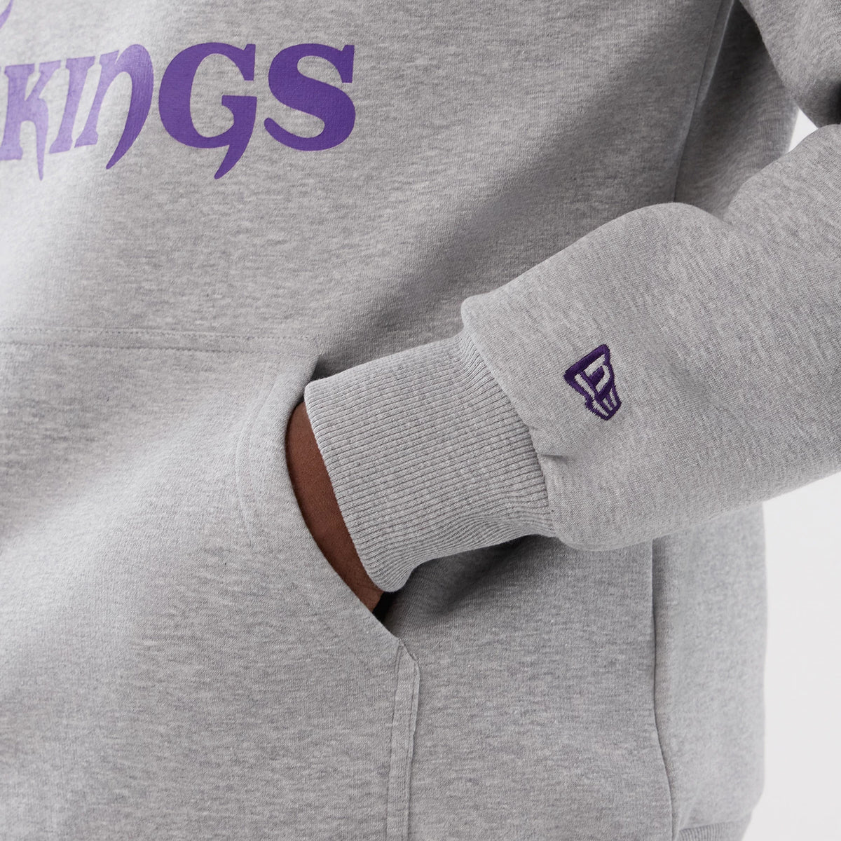 New Era Minnesota Vikings NFL International Series Games 2025 Grey Pullover Hoodie, three-quarter view showing the purple Vikings lettering across the chest and a purple embroidered New Era logo on the left cuff above the ribbed wrist.