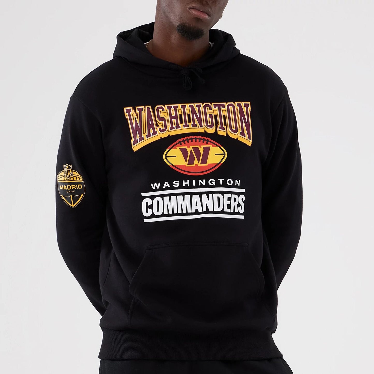 New Era Washington Commanders NFL International Series Games 2025 Black Pullover Hoodie, front view on-model showing large printed Washington and Commanders lettering on the chest and a Madrid Game badge on the left sleeve.