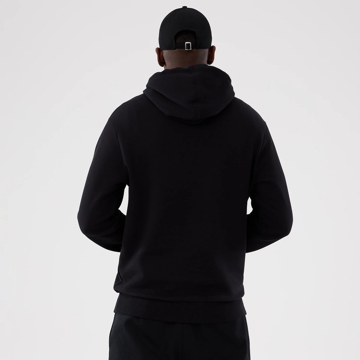 New Era Washington Commanders NFL International Series Games 2025 Black Pullover Hoodie, back view on-model showing a plain black hoodie with a relaxed fit, the hood resting on the shoulders and the ribbed hem at the waist.