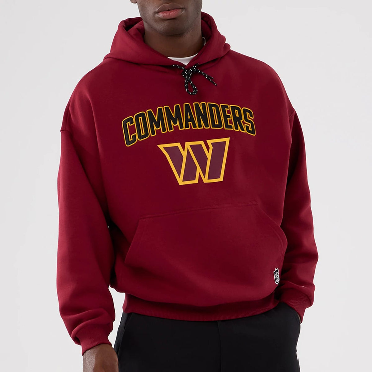 New Era Washington Commanders NFL International Series Games 2025 Dark Red Premium Pullover Hoodie, front view on a model showing the Commanders text and W logo across the chest with a black drawstring hood and a small patch logo near the hem.