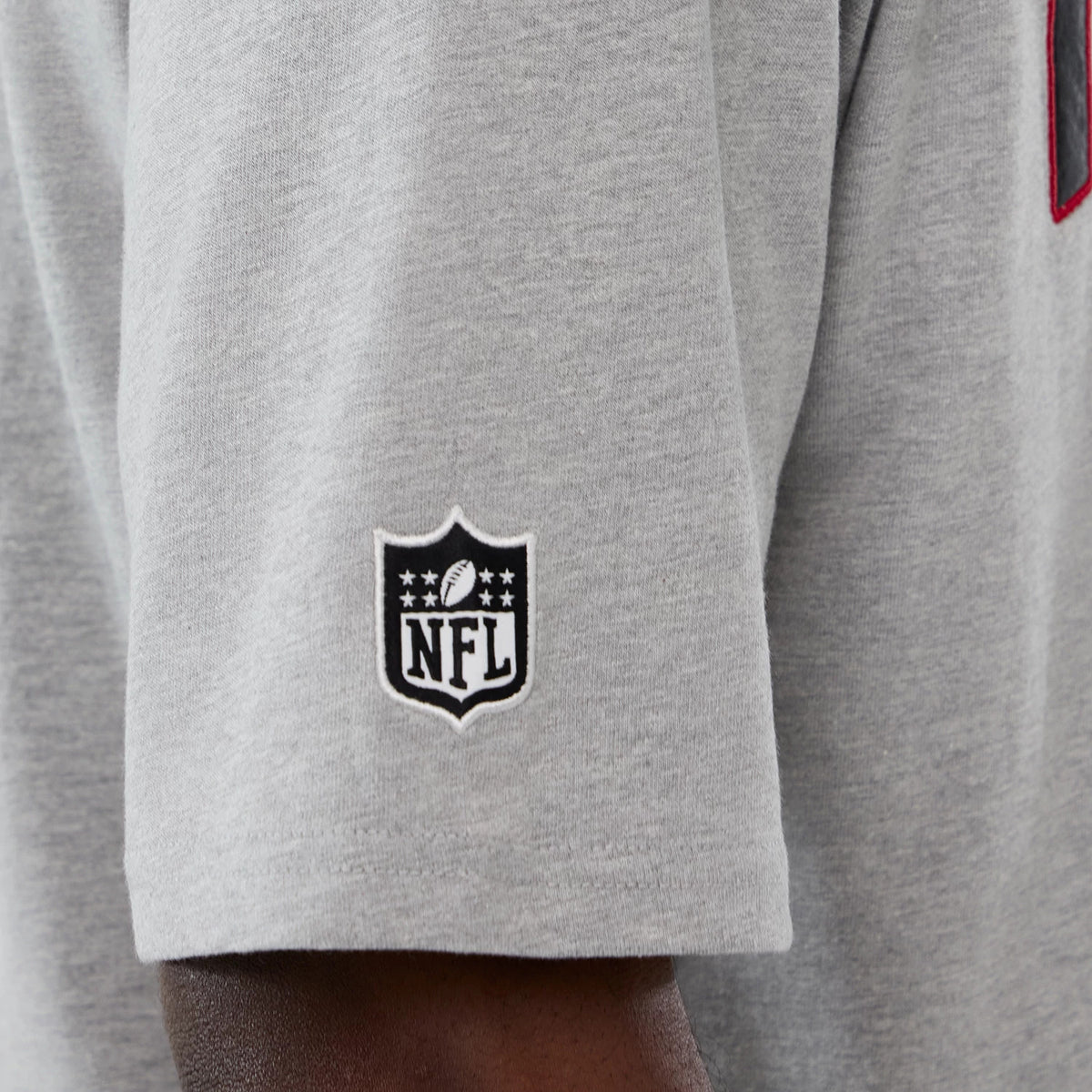 New Era Atlanta Falcons NFL International Series Games 2025 Grey Premium T-Shirt, side view showing the short sleeve with an embroidered black and white NFL shield logo near the hem against the light grey fabric.