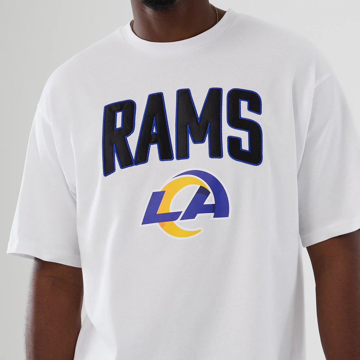 New Era LA Rams NFL International Series Games 2025 White Premium T-Shirt, front view showing large blue and black RAMS lettering across the chest with a printed blue and yellow LA logo beneath