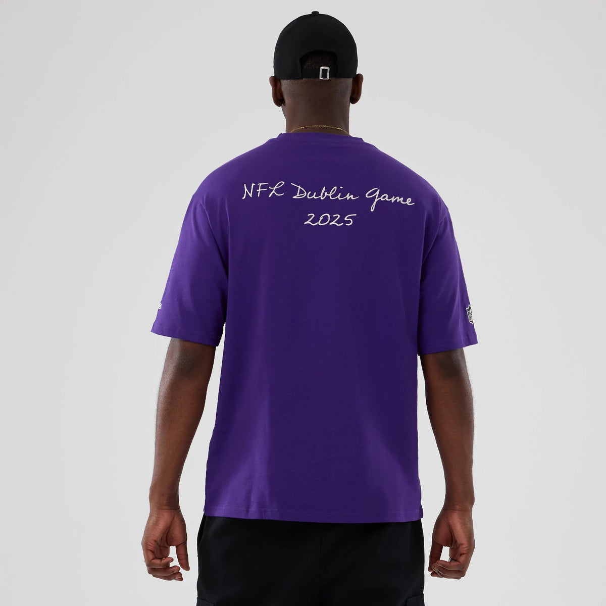 New Era Minnesota Vikings NFL International Series Games 2025 Purple Premium T-Shirt, back view on a model showing the white printed text NFL Dublin Game 2025 across the shoulders and an embroidered New Era logo on the left sleeve.