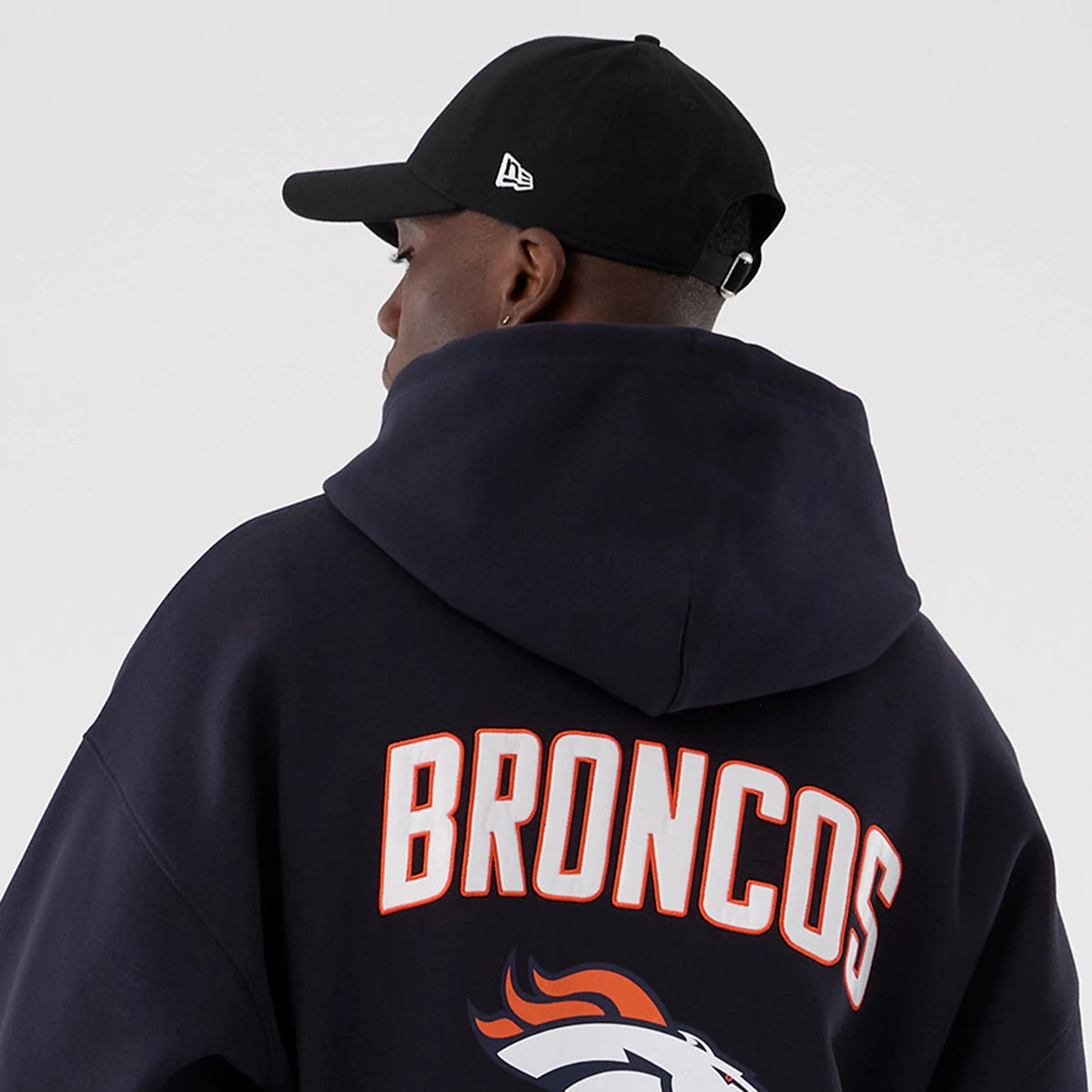 New Era Denver Broncos NFL International Series Games 2025 Navy Premium Pullover Hoodie, back view on a model showing large Broncos lettering across the shoulders, the Denver Broncos logo beneath.