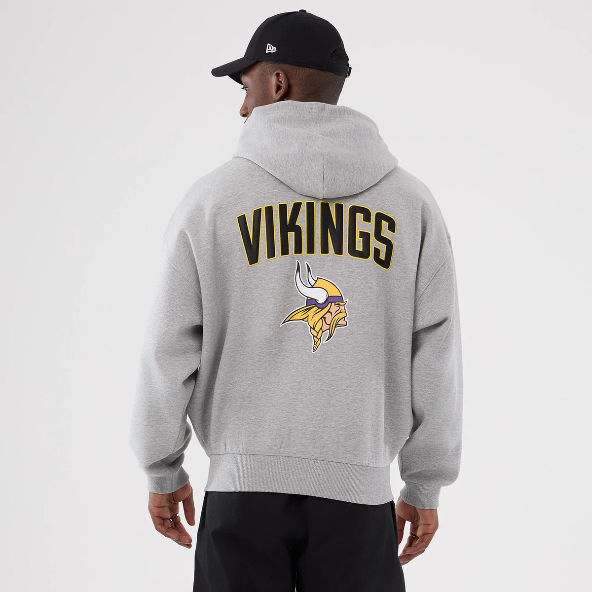 New Era Minnesota Vikings NFL International Series Games 2025 Grey Premium Pullover Hoodie, back view on-model displaying VIKINGS lettering and team logo printed in black and yellow across the upper back above the ribbed hem.