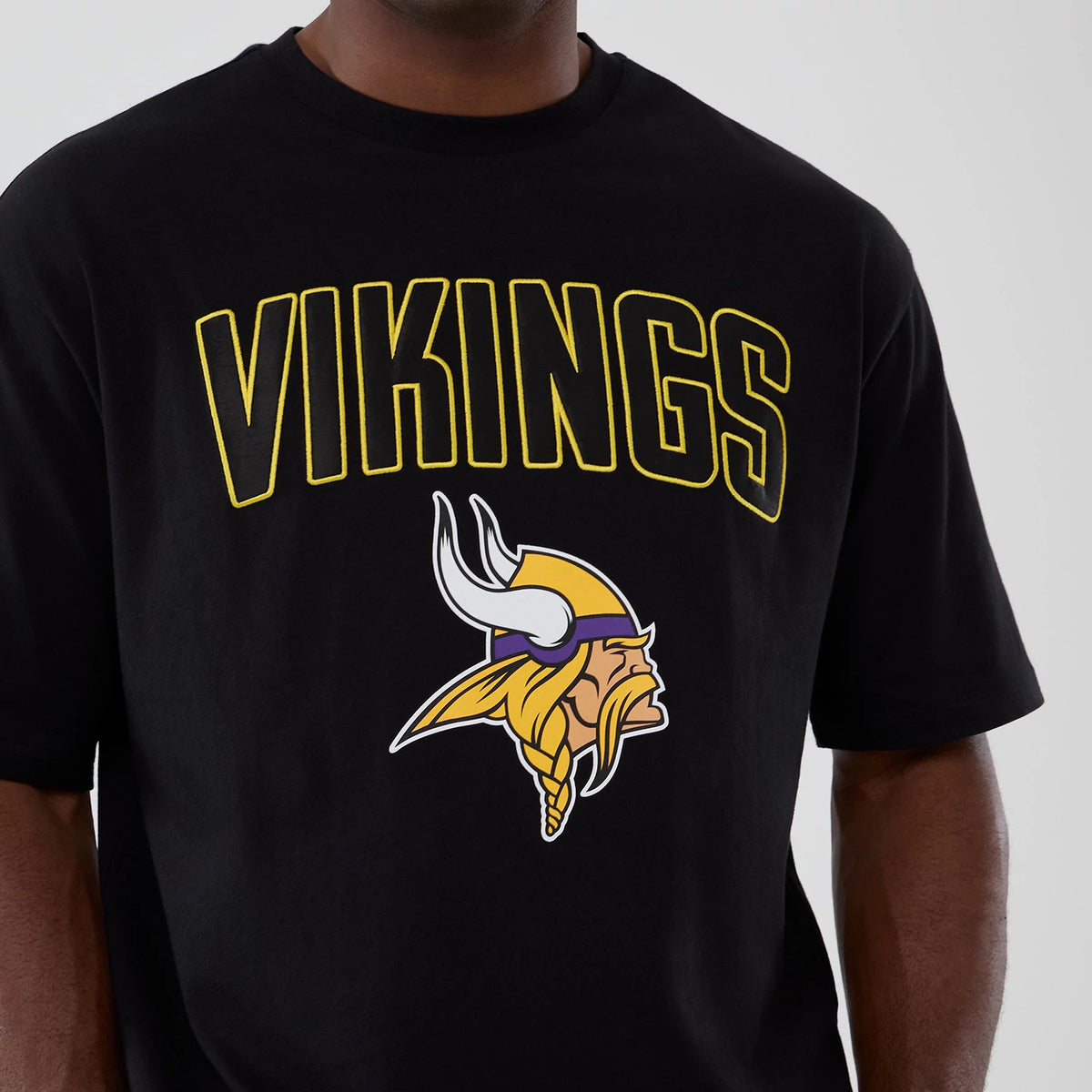 New Era Minnesota Vikings NFL International Series Games 2025 Black Premium T-Shirt, front view showing the yellow outlined VIKINGS text and a large printed Viking head logo centred on the chest against the black fabric.