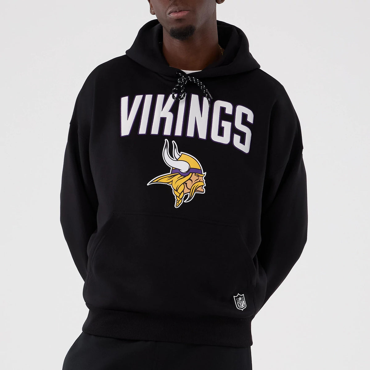 New Era Minnesota Vikings NFL International Series Games 2025 Black Premium Pullover Hoodie, front view on a model showing white VIKINGS lettering and the team’s horned helmet logo printed on the chest.