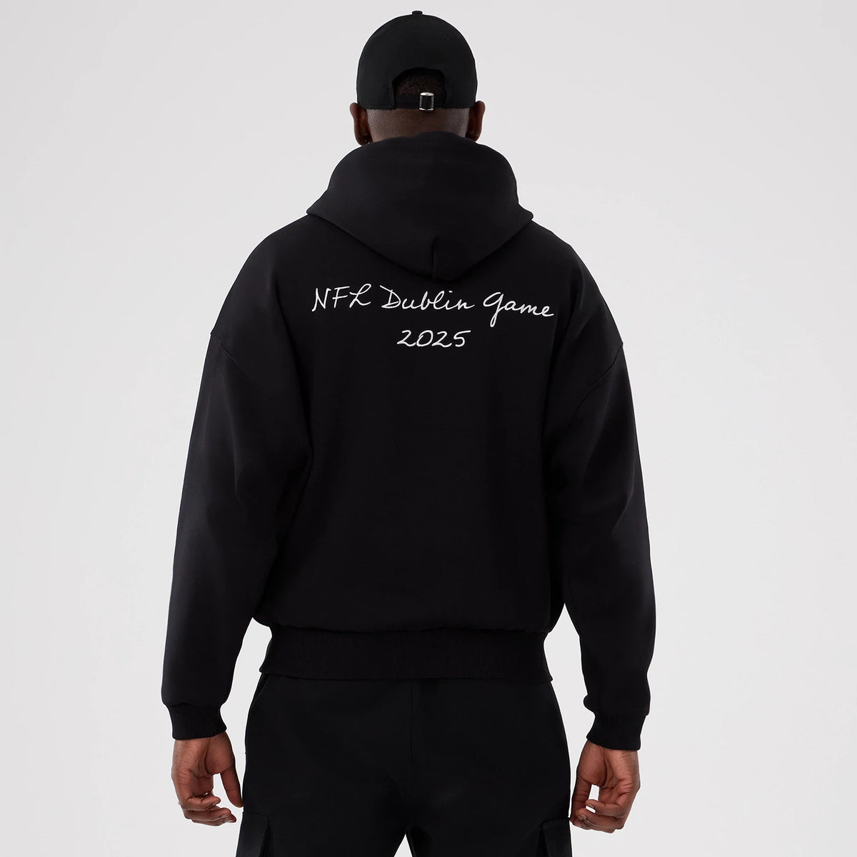New Era Minnesota Vikings NFL International Series Games 2025 Black Premium Pullover Hoodie, back view on-model showing white script lettering reading NFL Dublin Game 2025 across the upper back of the black hoodie.