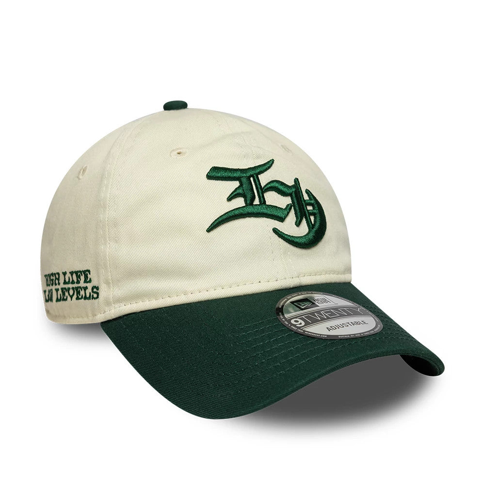 EDWIN x New Era Cream 9TWENTY Adjustable Cap, three-quarter view showing the green embroidered script logo on the front panel, green visor with a 9TWENTY size sticker, and HIGH LIFE LOW LEVELS lettering on the side.