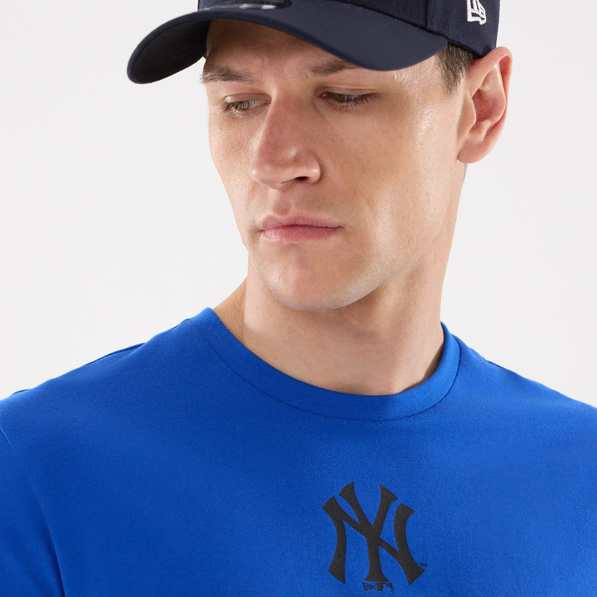 New Era New York Yankees MLB Blue T-Shirt, front view on-model showing a black Yankees logo centrally printed on the chest, paired with a matching navy cap that features an embroidered New Era logo on the side.