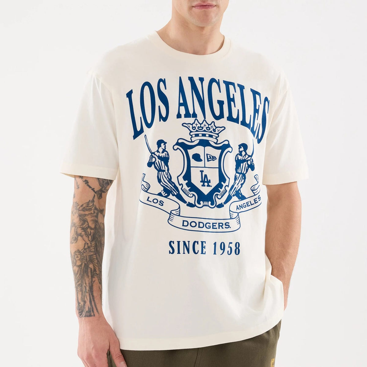 New Era LA Dodgers MLB Life Graphic Light Beige T-Shirt, front view on a model showing a large blue printed crest with Los Angeles lettering above, detailed graphics including the LA logo at the centre, and Since 1958 below.