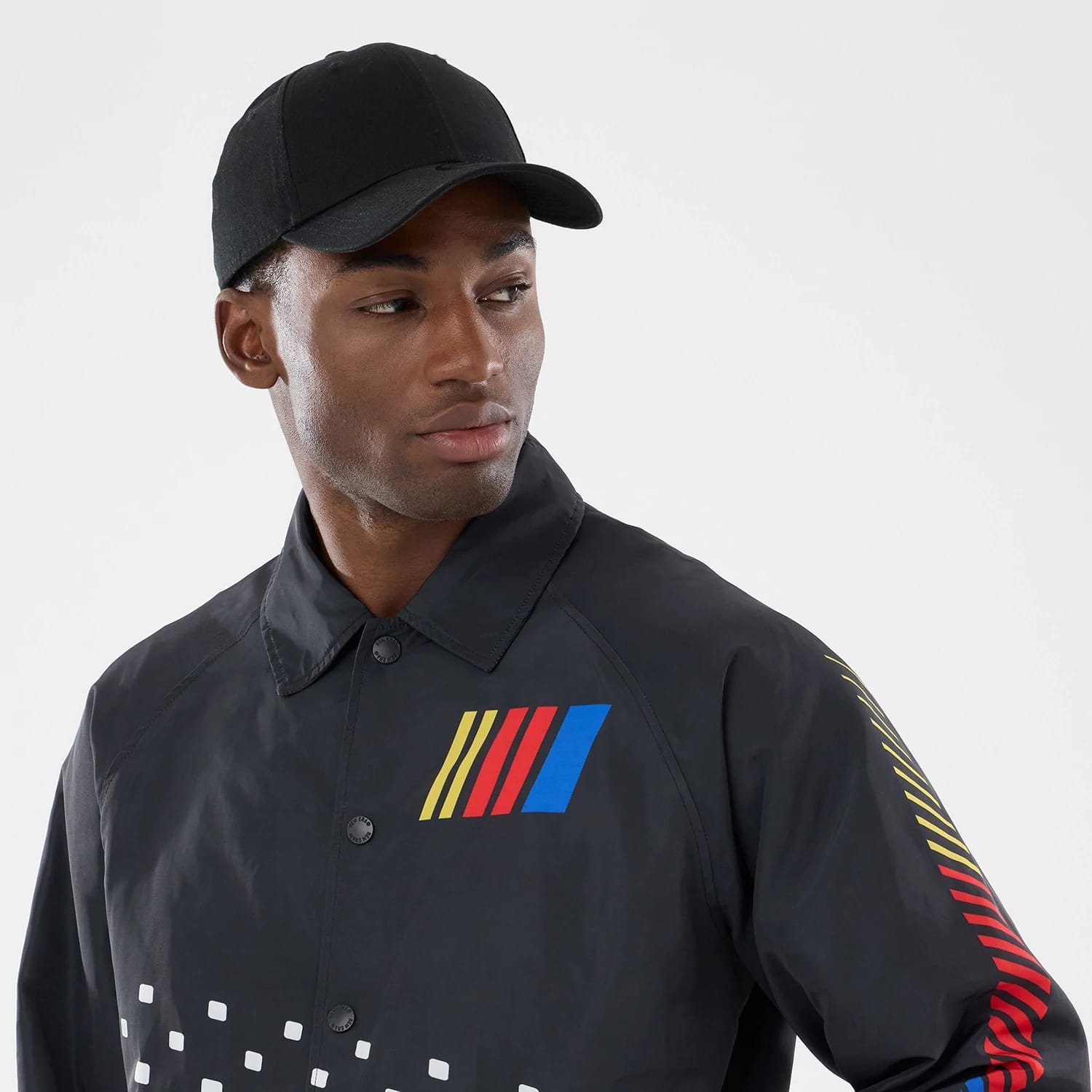 New Era Nascar Logo Black Jacket, front view on a model featuring a yellow, red, and blue embroidered Nascar logo on the chest, a series of white square prints at the bottom, and striped down the left sleeve.