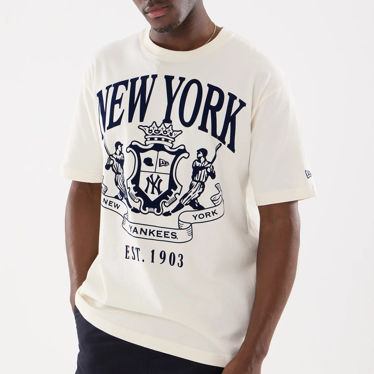 New Era New York Yankees MLB Life Graphic Light Beige T-Shirt, front view on a model showing a navy New York Yankees crest with intricate team graphics across the chest, established date 1903 below, and a small embroidered New Era logo on the sleeve.