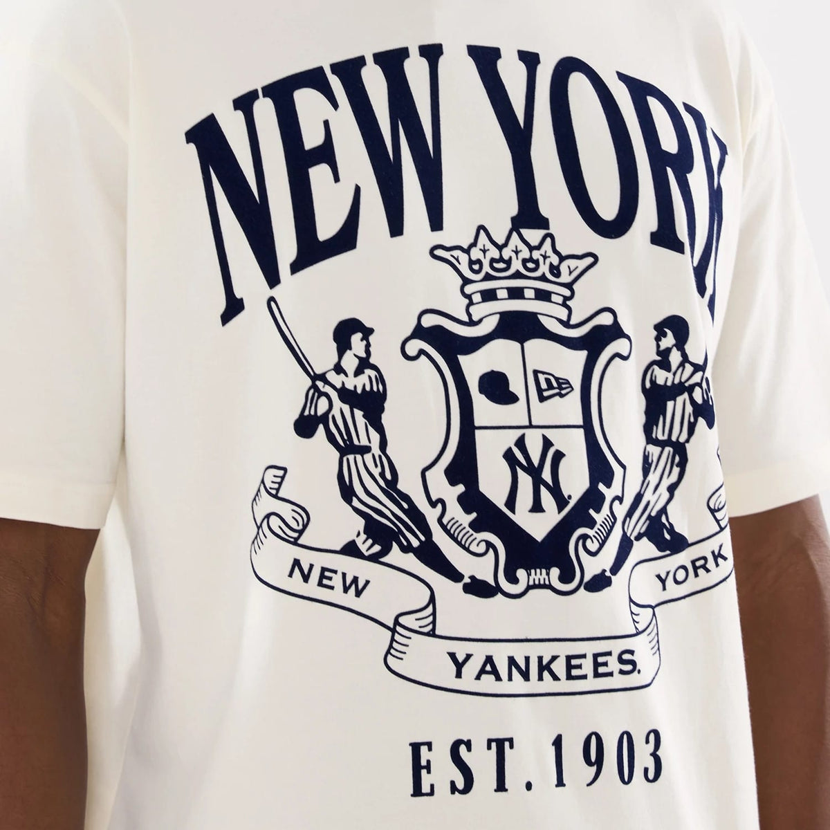 New Era New York Yankees MLB Life Graphic Light Beige T-Shirt, front view showing a large printed crest centred on the chest with New York lettering at the top, dynamic illustrations of baseball players, and Est. 1903 text below.