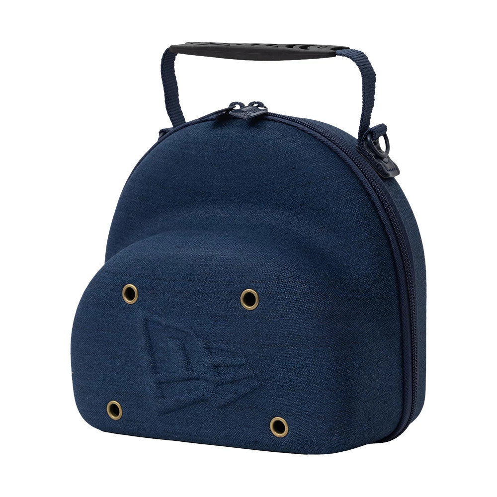 New Era Denim Navy 2Pk 59FIFTY Cap Carrier, side view showing a rounded navy shell with a zip closure along the edge, a black handle on top, a debossed New Era logo, and eyelets on one side.