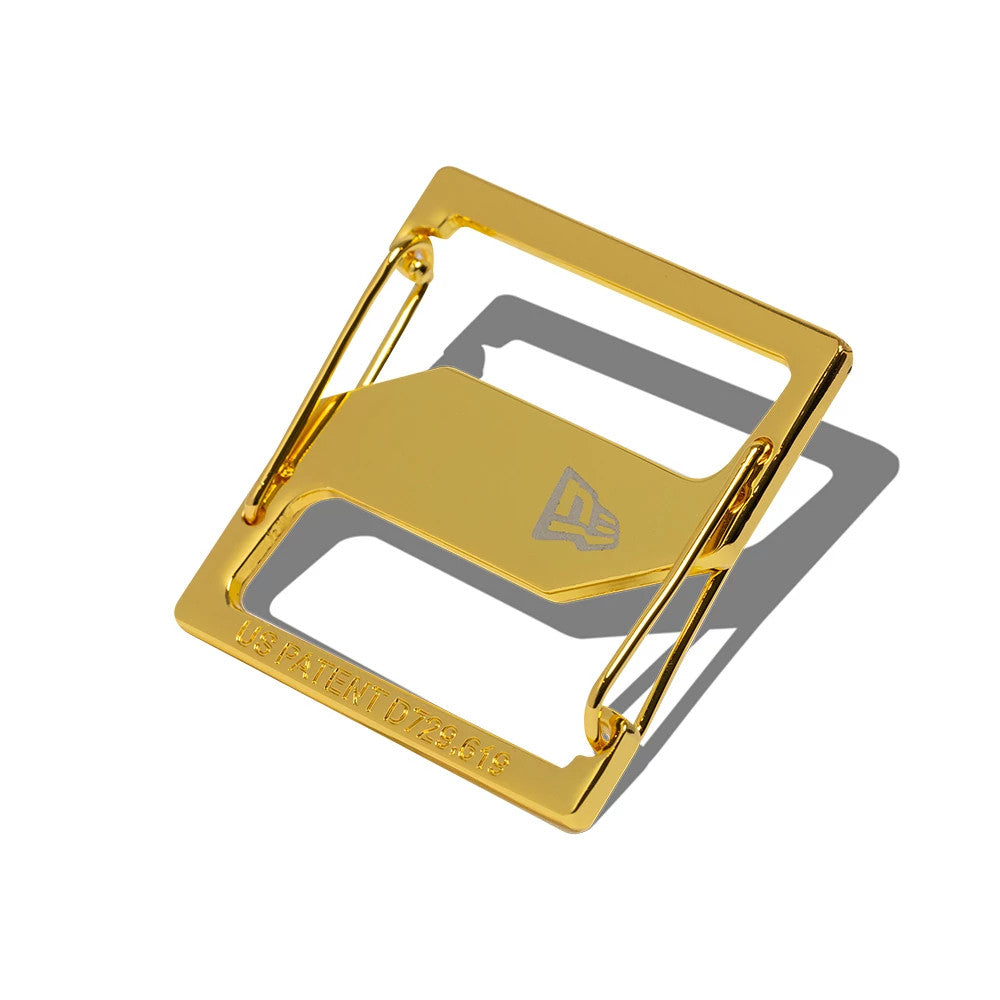 New Era Gold Cap Clip, angled view showing a rectangular design with a polished gold finish, featuring the New Era flag logo engraved on the central panel and the US patent number displayed along the bottom edge.