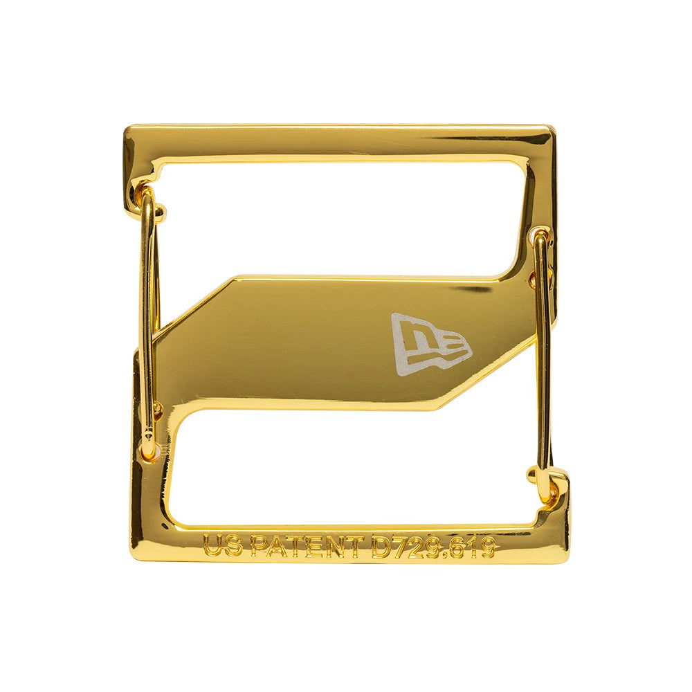 New Era Gold Cap Clip, close-up showing a rectangular gold frame with a central bar that features the New Era flag logo engraved in white, accompanied by a patent number inscription along the bottom edge.