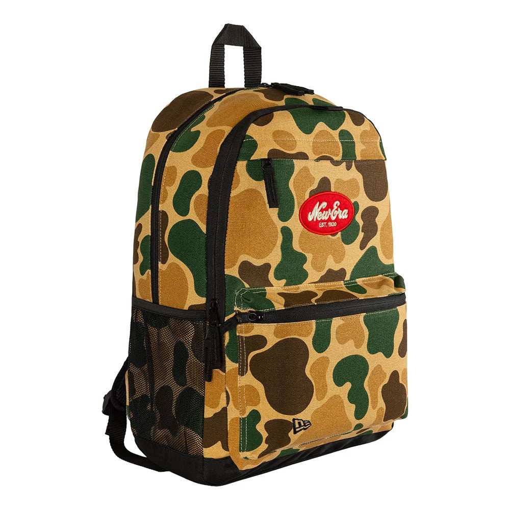 New Era Camo Light Beige Delaware Backpack, three-quarter view showcasing the camouflage pattern, a large front pocket with a black zip, a red embroidered New Era EST. 1920 logo centred above the pocket, and a black mesh side pocket.