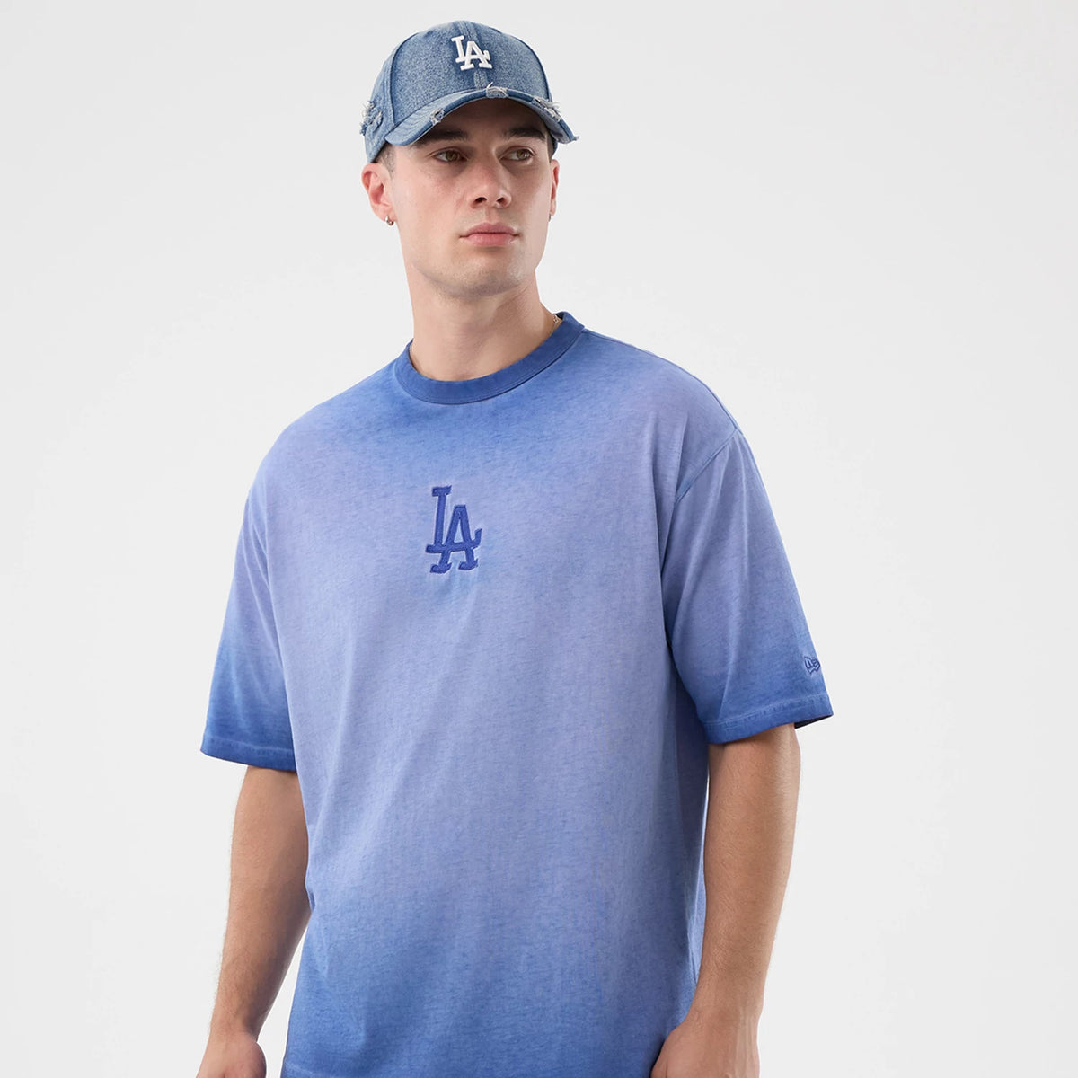 New Era LA Dodgers MLB Washed Logo Pastel Blue T-Shirt, front view on-model showing the gradient blue colour with an embroidered LA logo in the centre of the chest, short sleeves, and a small New Era logo embroidered on the left sleeve.