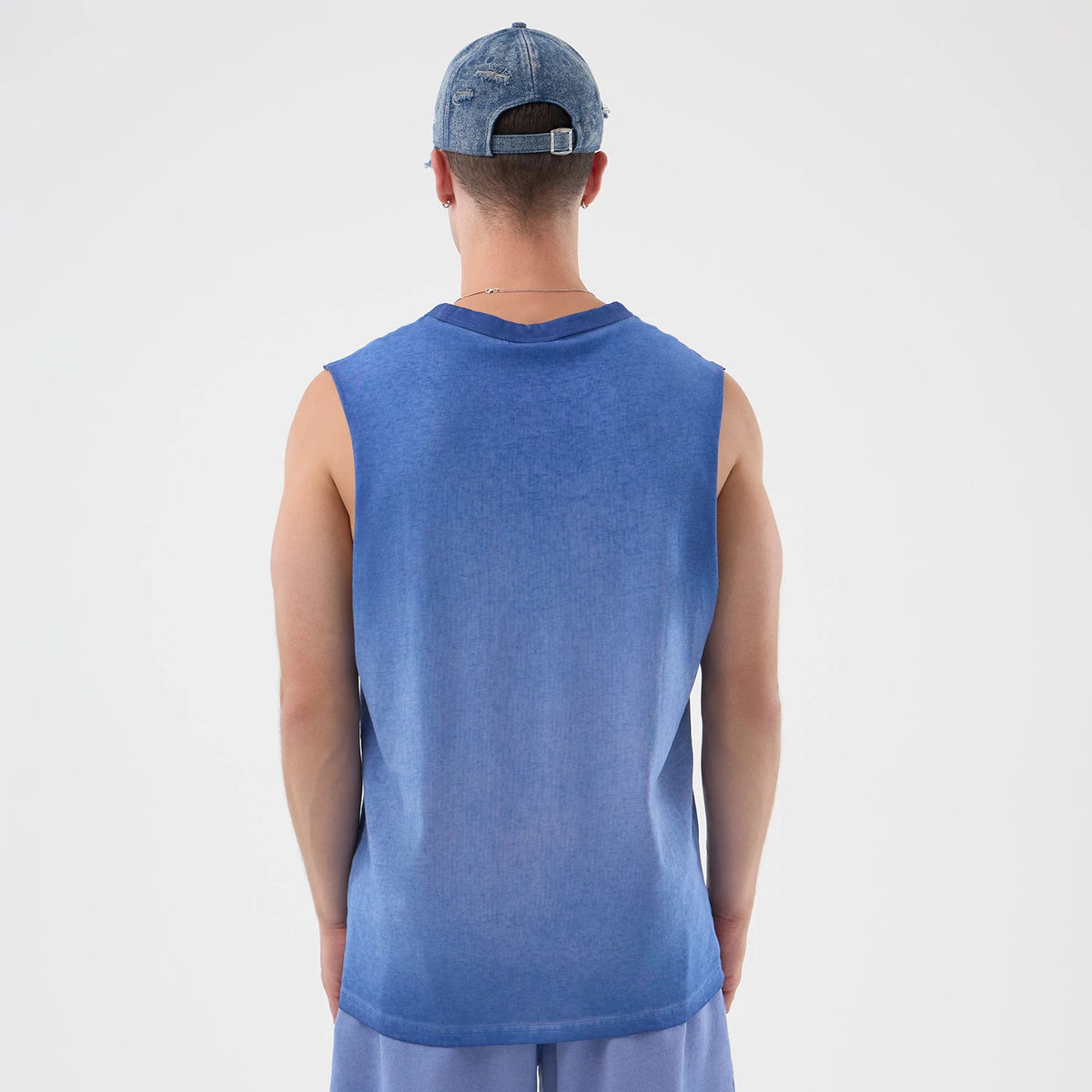 New Era LA Dodgers MLB Washed Logo Pastel Blue Vest, back view on a model showcasing a sleeveless design with a soft blue gradient finish, plain hem, and ribbed neckline, pairing with light shorts and a distressed denim cap.
